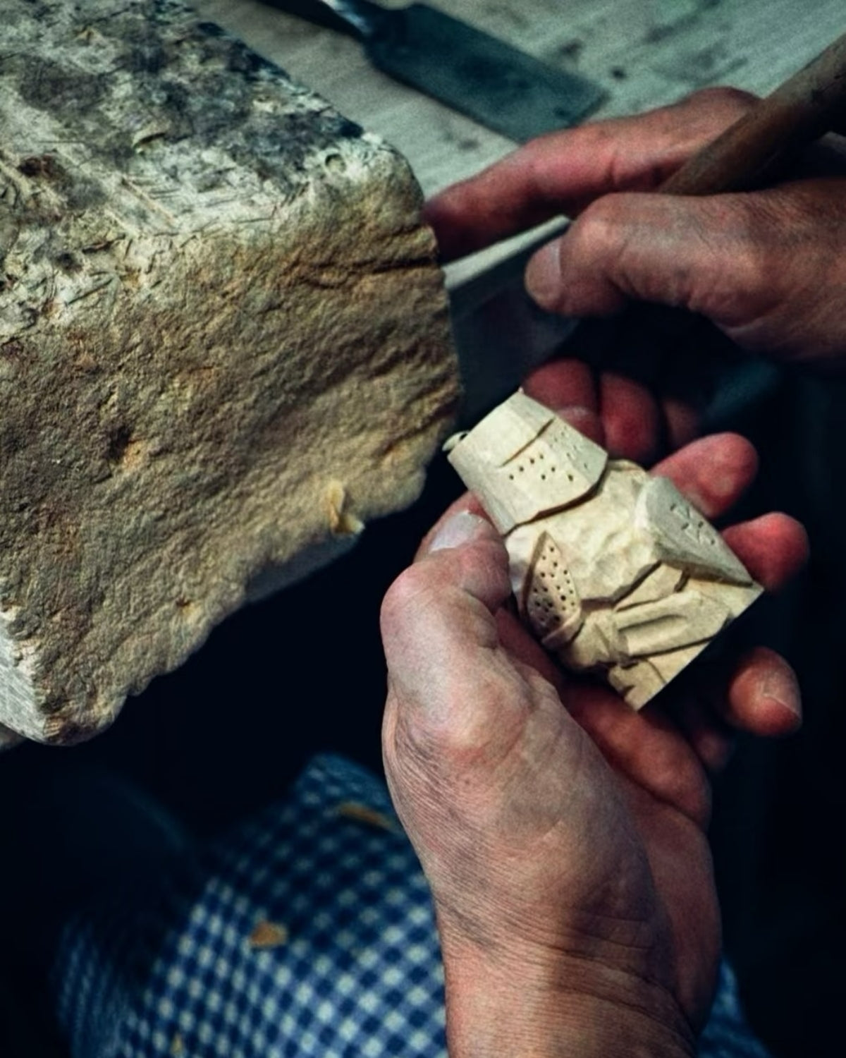 An artisan holding a small wooden carving while refining its details