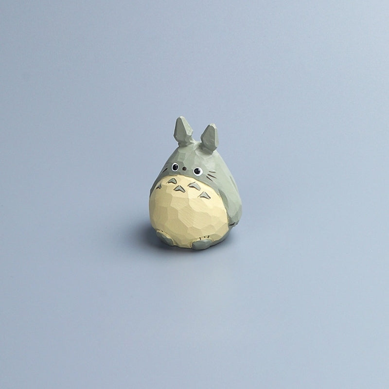 Hand-carved wooden Totoro figurine with painted details, standing alone on a light blue background.