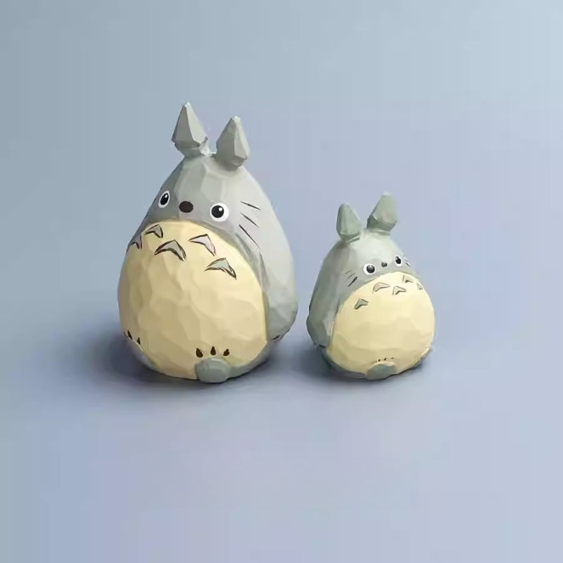 Pair of hand-carved wooden Totoro figurines displayed side by side on a soft gray-blue surface.